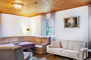 A living room with a wooden ceiling, a sofa, a table with a purple tablecloth, and a painting on the wall. - Holiday Home 'Schenum' with Private Terrace and Private Garden (Jever)