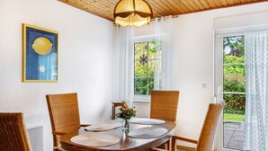 Ein Essbereich mit Holztisch, Korbstühlen, einer Pendelleuchte und einem Fenster mit Blick ins Grüne.