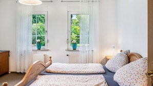 Ein Schlafzimmer mit zwei Betten, einem Fenster mit Blick auf Grünflächen, einem Heizkörper und einem Nachttisch mit einer Lampe.
