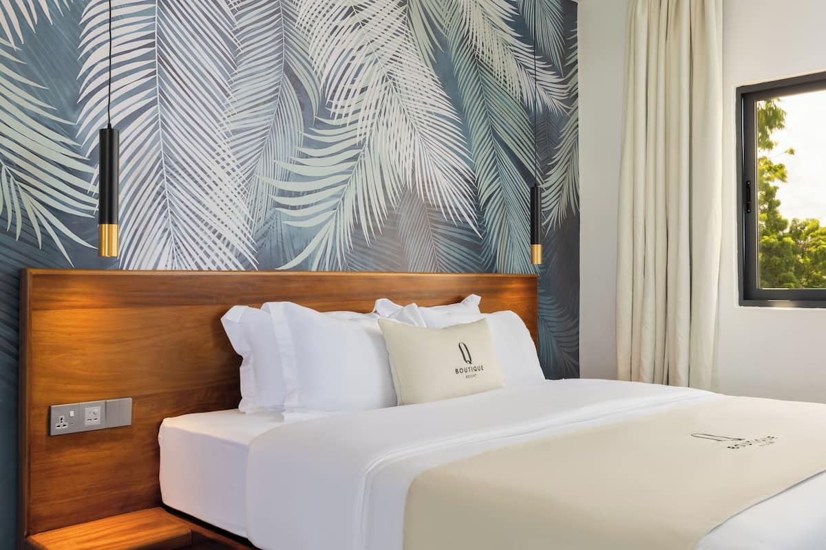 Une chambre d’hôtel avec une tête de lit en bois, du linge de lit blanc et un mur orné d’un motif de feuilles de palmier.