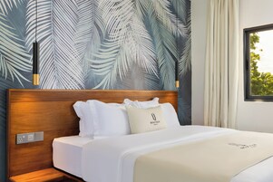 Habitación de hotel con cabecera de madera, ropa de cama blanca y pared con estampado de hojas de palma.