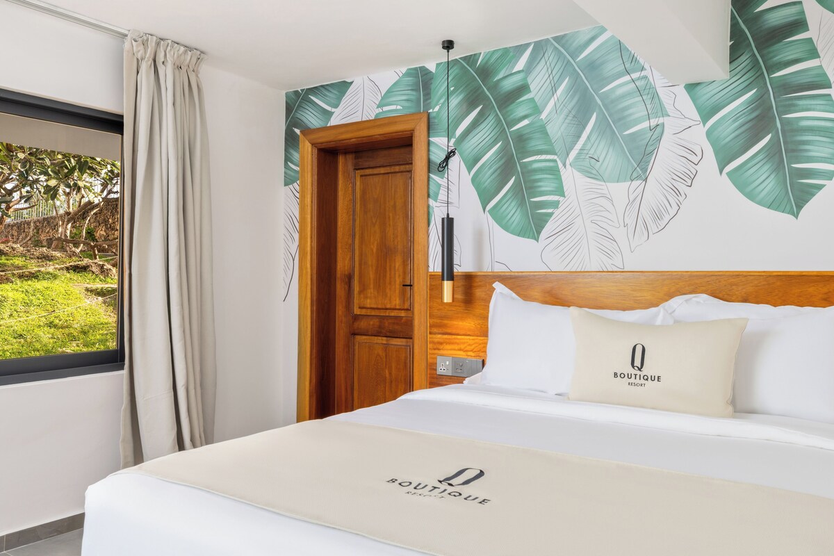 Une chambre d’hôtel avec un lit, une porte en bois, une fresque murale et une fenêtre avec des rideaux.