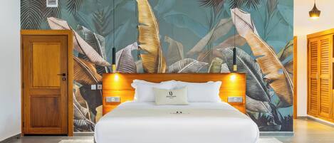 A hotel room with a large bed, wooden headboard, and a tropical leaf-patterned wall.