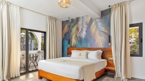 Una habitación de hotel moderna con una cama grande, cabecera de madera, un mural de hojas tropicales y un balcón con vistas a palmeras.
