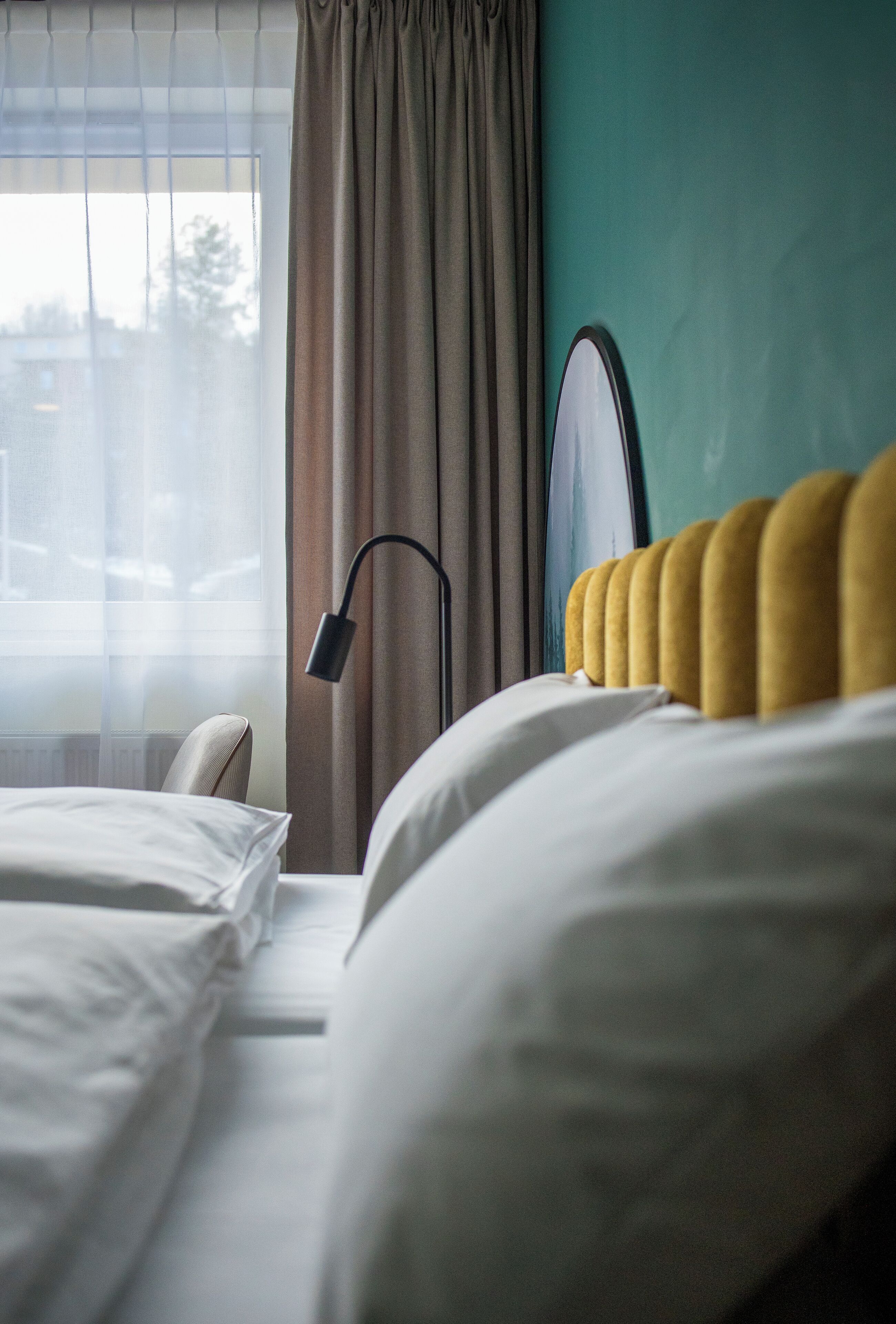 Et hotelværelse med en seng, en stol, en lampe og udsigt ud ad et vindue med gardiner.