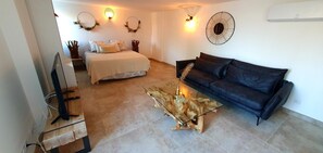 Un salon comprenant un lit, un canapé en cuir noir, une table basse en verre et un climatiseur fixé au mur.