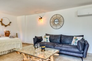 Una sala de estar con una mesa de centro de vidrio, un sofá oscuro, un espejo montado en la pared y una guirnalda decorativa.
