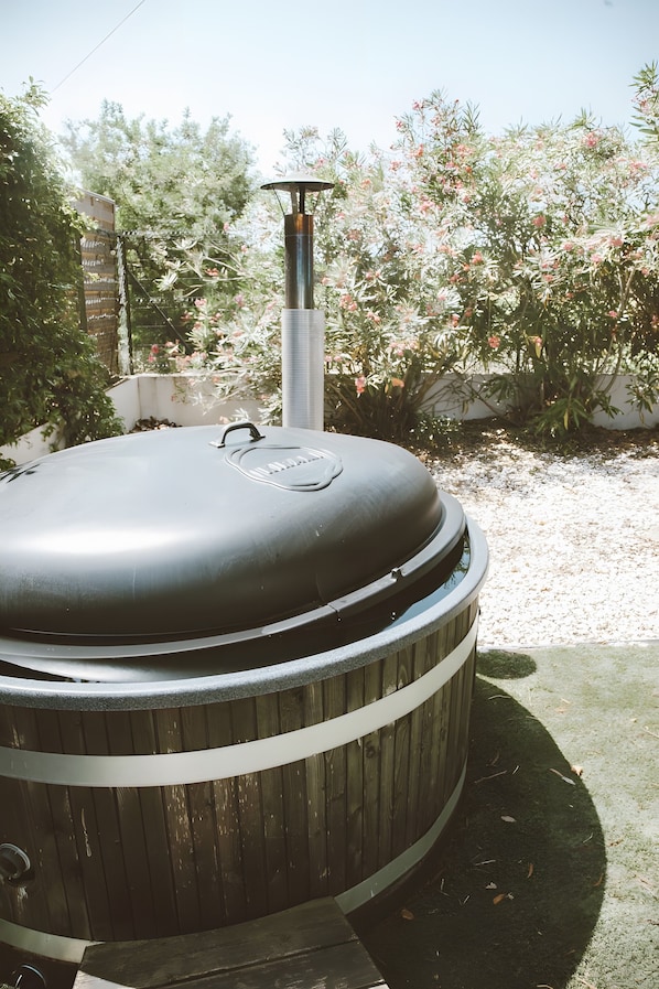Un barbecue de forme cylindrique, doté d’une cheminée, installé à l’extérieur, avec un jardin en arrière-plan.
