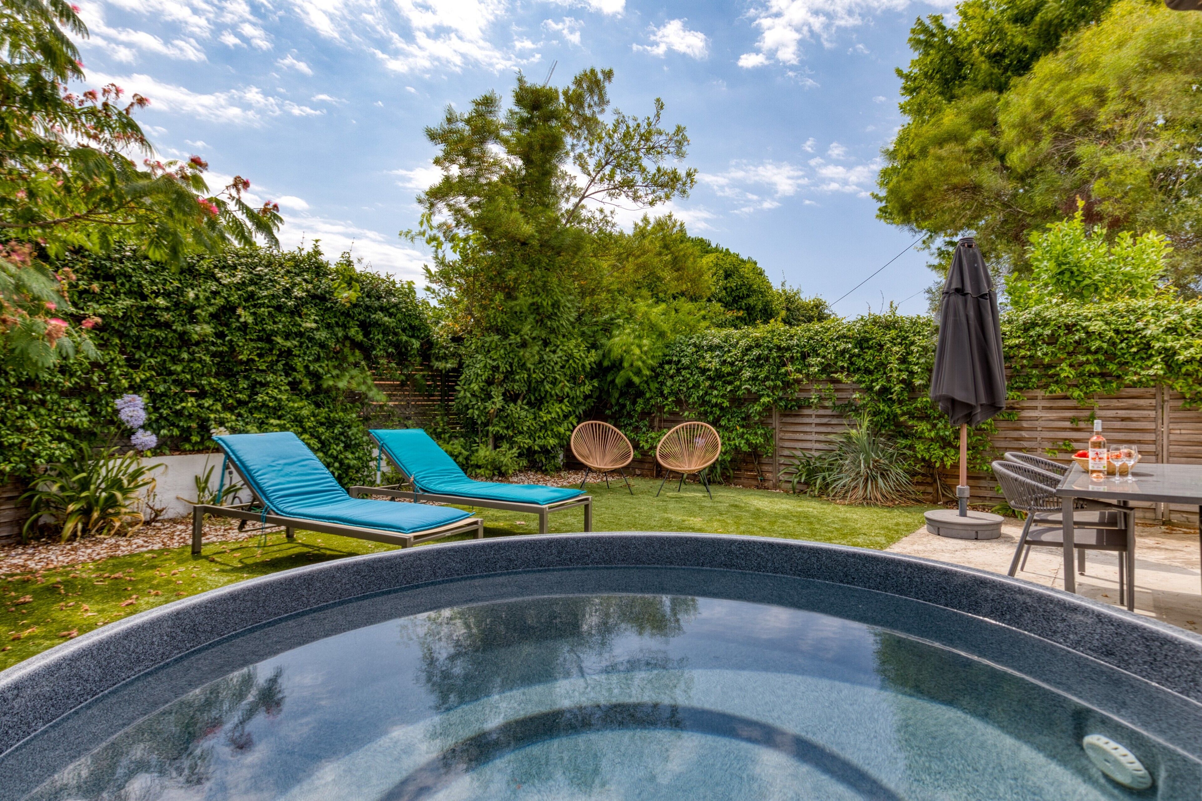 Un jardin avec une piscine, deux chaises longues, une table avec des chaises et une clôture en bois.