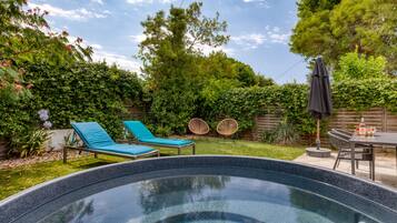 Un jardin avec une piscine, deux chaises longues, une table avec des chaises et une clôture en bois.