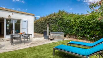 Un jardin avec une terrasse, un jacuzzi et des chaises longues.