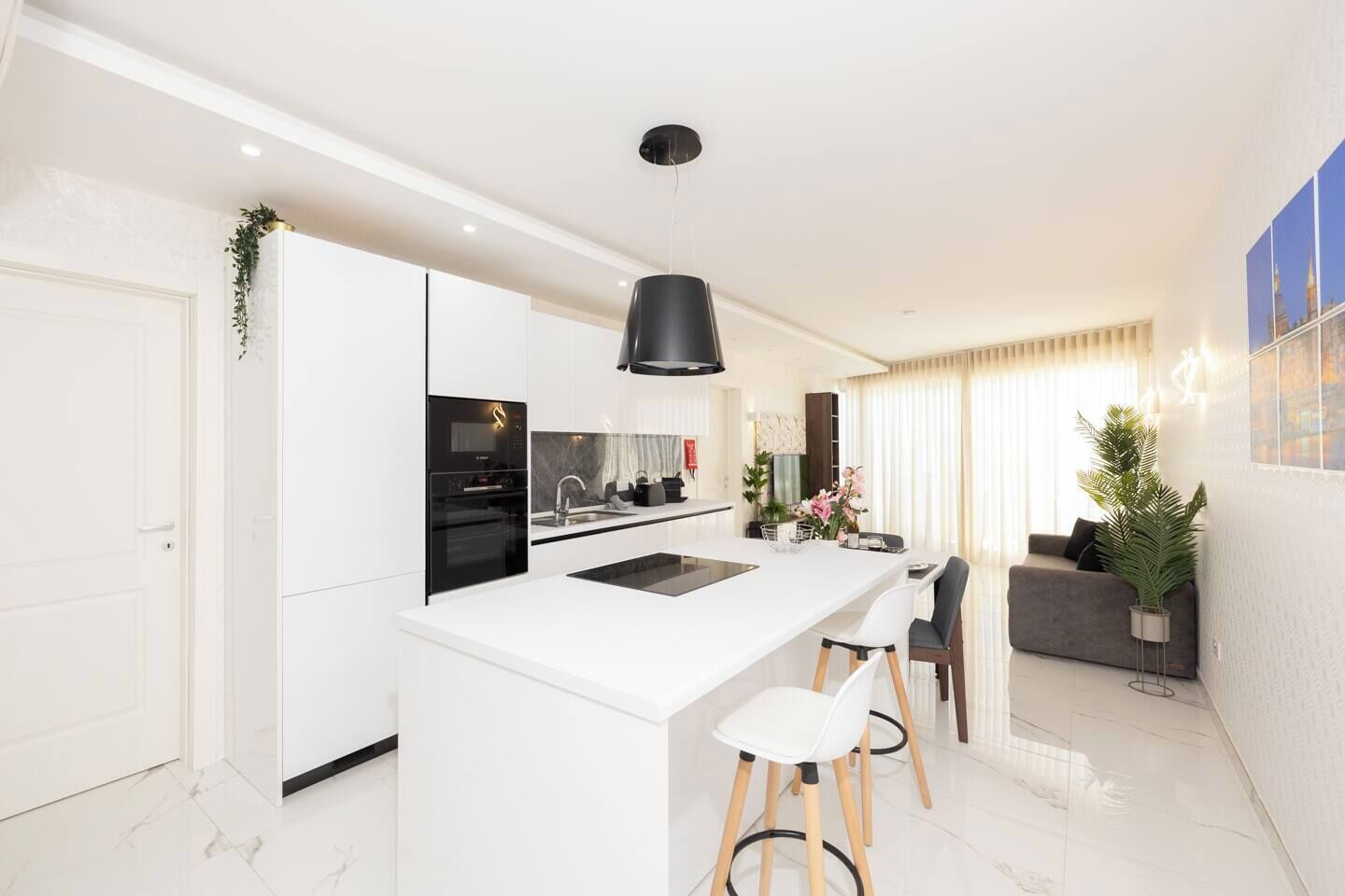 A modern kitchen with white cabinetry, a black pendant light, and a central island with stools.