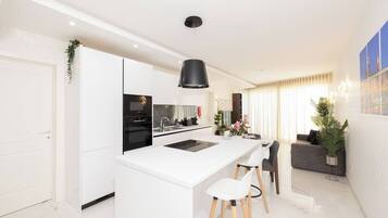 A modern kitchen with white cabinetry, a black pendant light, and a central island with stools.