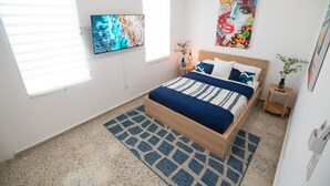 Un dormitorio con una cama, un televisor, un cuadro y una ventana.