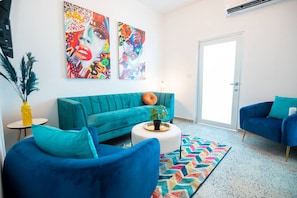A modern living room with a teal sofa, blue armchairs, and colorful artwork on the walls.