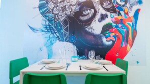 Una mesa de comedor dispuesta con platos, cubiertos y vasos, con un mural colorido de fondo.