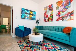 Una sala de estar moderna con un sofá color esmeralda, un sillón azul y obras de arte coloridas en las paredes.