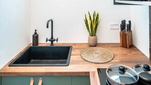 A modern kitchen with a wooden countertop, a black sink, a potted plant, a knife block, and a microwave.
