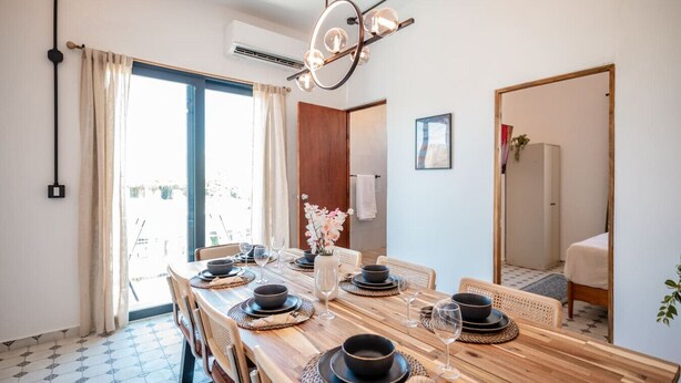 A dining area with a wooden table set for four, surrounded by wicker chairs.