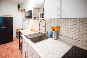 A kitchen with a black refrigerator, a sink with a modern faucet, a microwave above the counter, and a hexagonal tile backsplash. - Casa Flores「UNIT 2「Amapola」Walk To Beach (San Juan)