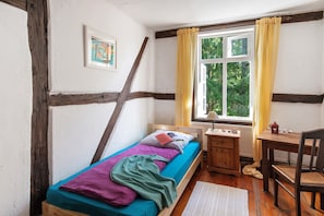 Een kamer met een bed, een bureau, een stoel, een raam met gordijnen en een radiator.