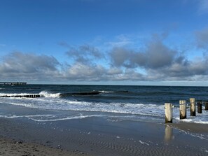 Een strand met golven, een houten steiger en bewolkte lucht.