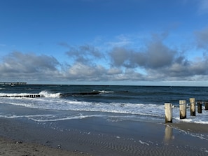 Een strand met golven, een houten steiger en bewolkte lucht.