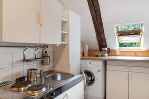 A compact kitchen with a washing machine, a window with blinds, and a wooden beam ceiling. - Apartment 'Lemon Attic' with Shared Terrace, Shared Garden and Wi-Fi (Wardow Ortsteil Polchow)