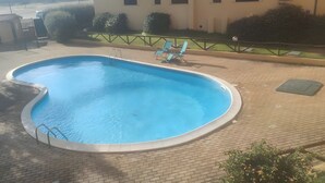 A swimming pool with a curved edge, a metal ladder, and two lounge chairs. - Apartment 'Olbia Comfort' with Shared Pool, Balcony and Air Conditioning (Olbia)