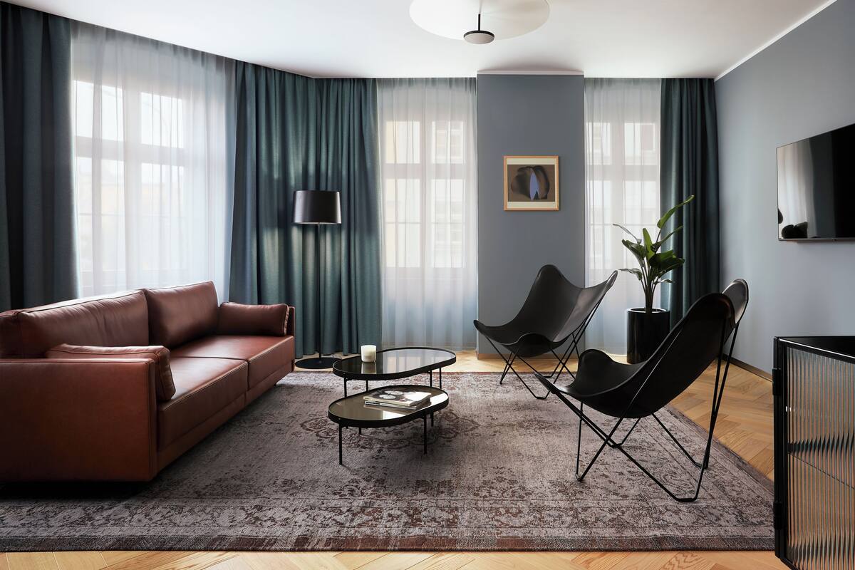A modern living room with a leather sofa, a glass coffee table, and two black chairs.