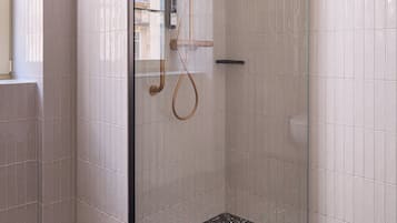 A glass-enclosed shower with a handheld showerhead and a rain shower head, tiled walls, and a speckled floor.