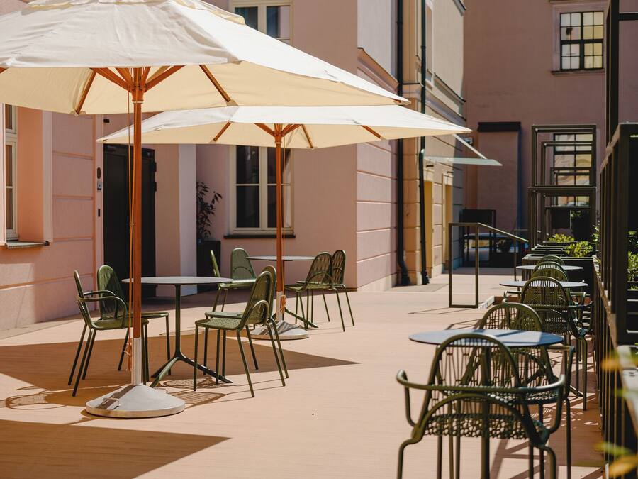 An outdoor seating area with tables and chairs, a large umbrella, and a building facade in the background.