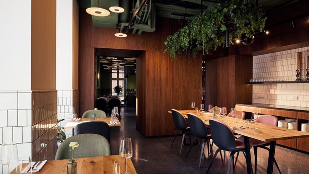 L’intérieur d’un restaurant avec des tables en bois, des chaises noires et des plantes suspendues.