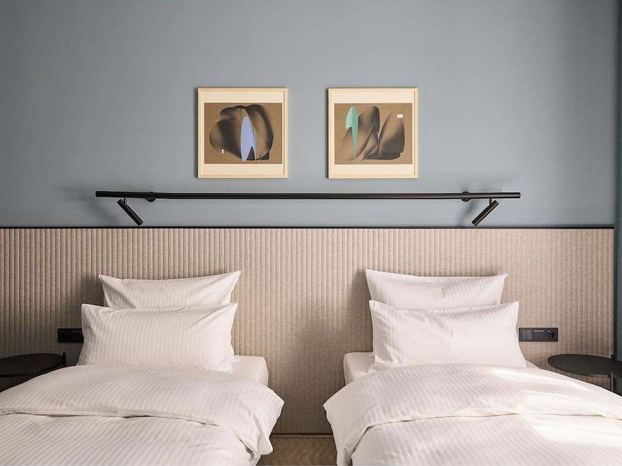 Een hotelkamer met twee bedden, een hoofdeinde, een tafeltje en twee foto's in lijsten aan de muur.