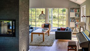 A spacious living room with a fireplace, large windows, a bookshelf, and a modern chandelier. - Beautiful home in Ejstrupholm with WiFi (Ejstrupholm)
