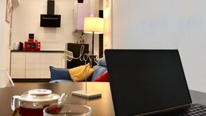 Un espace de vie moderne avec un ordinateur portable posé sur une table, un néon mural et un coin cuisine à l’arrière-plan.