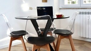 Un coin repas comprenant une table ronde, trois chaises, un ordinateur portable et une étagère décorative ornée de cadres avec des photos.