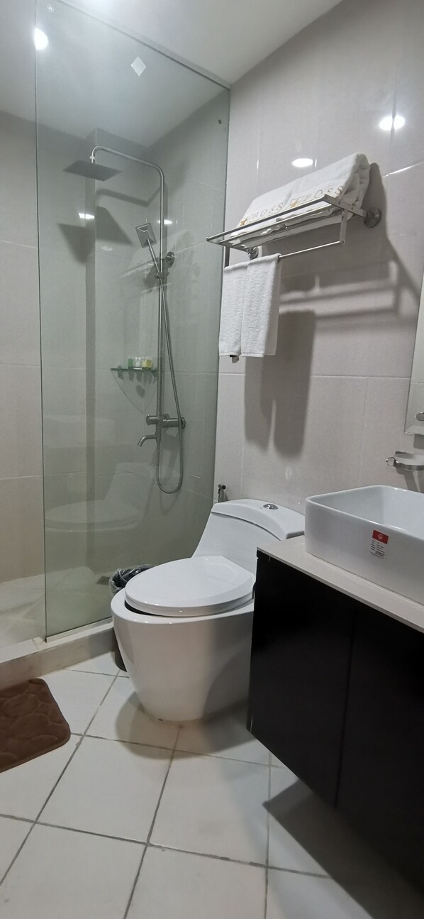 Une salle de bain moderne avec une douche à parois de verre, des toilettes blanches, un lavabo avec un miroir et un porte-serviettes.