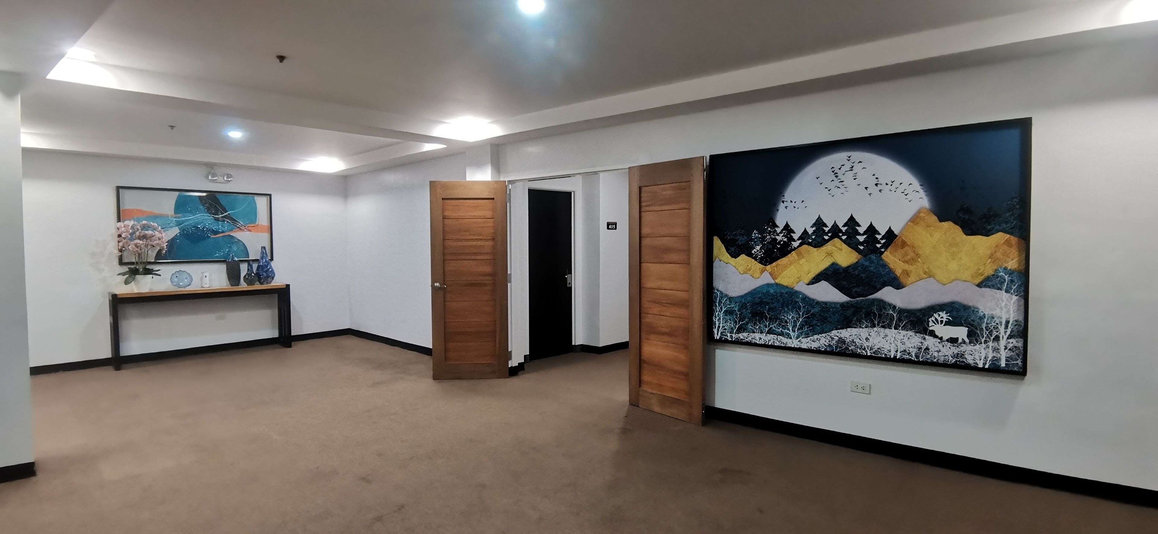 Een gang met kunst aan de wanden, een bankje met een vaas, en een deur naar een andere kamer.