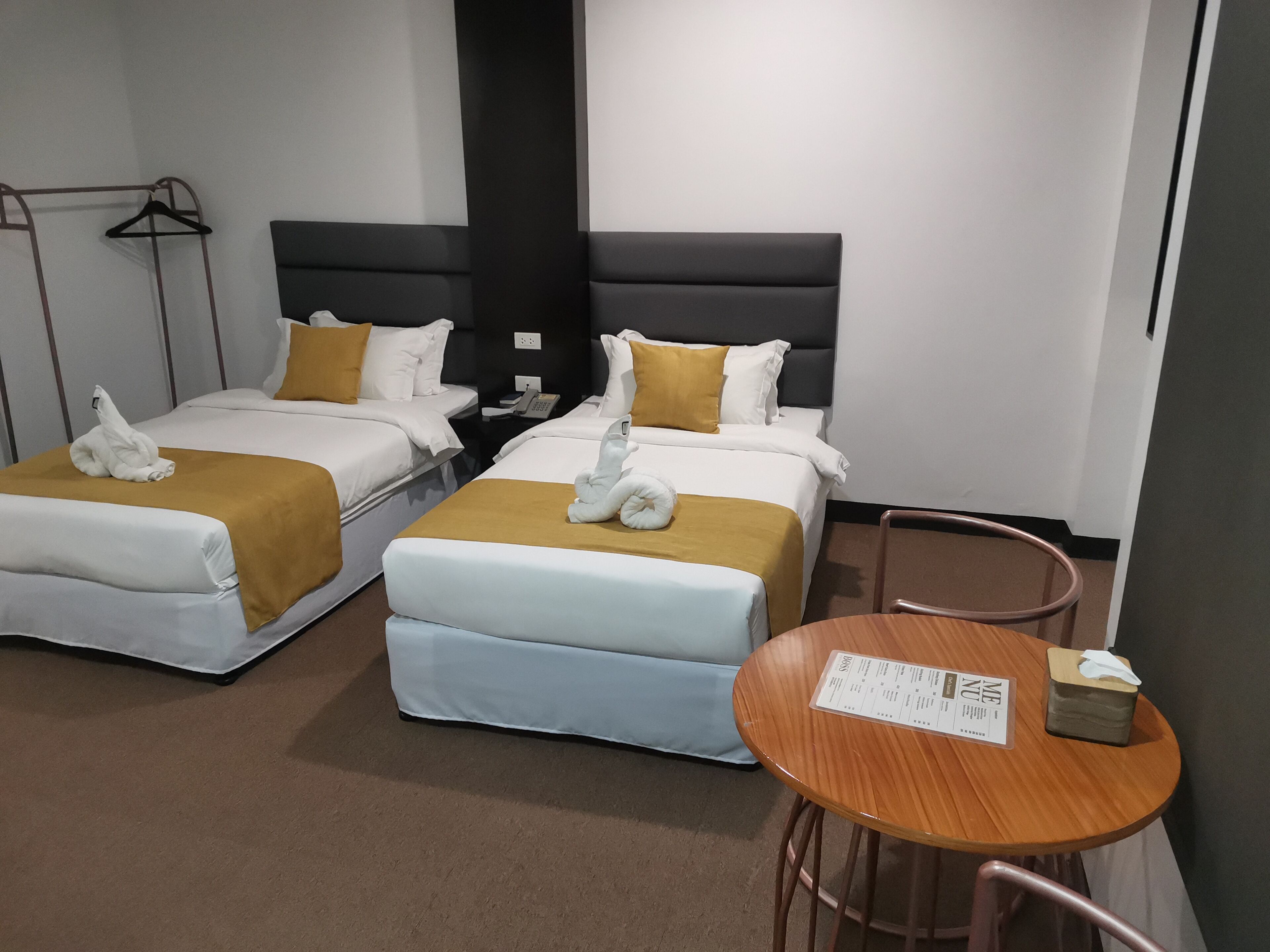 Una habitación de hotel con dos camas, cada una con una colcha blanca y dorada, y una mesa de madera con un menú.