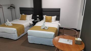 Una habitación de hotel con dos camas, cada una con una colcha blanca y dorada, y una mesa de madera con un menú.