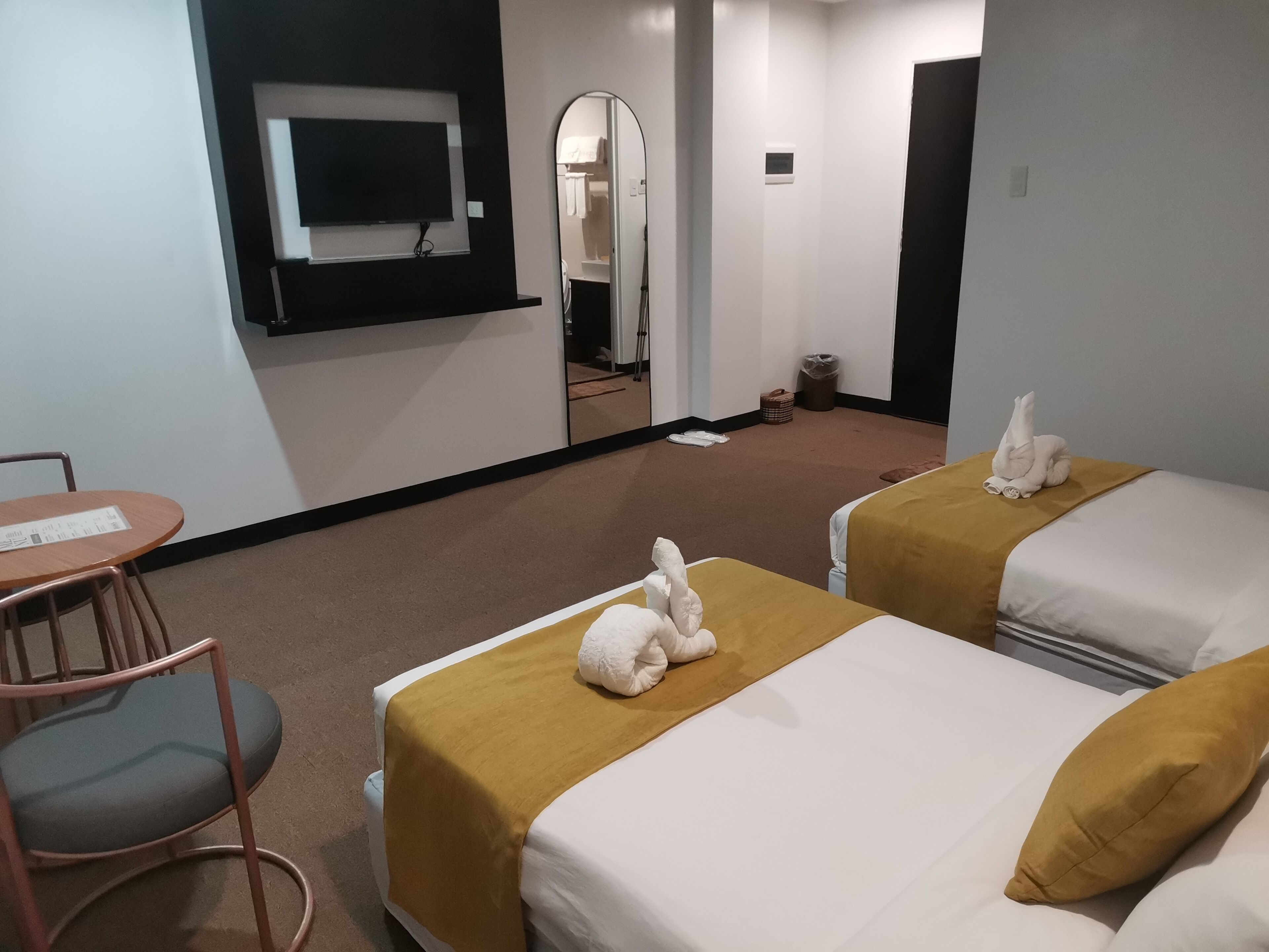 Ein Hotelzimmer mit zwei Betten, einem an der Wand befestigten Fernseher, einem kleinen Tisch und einem Sessel.