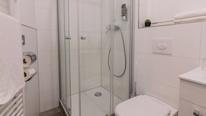 Un baño moderno con ducha de vidrio, azulejos blancos, inodoro y una pequeña planta en maceta sobre el mueble de tocador.