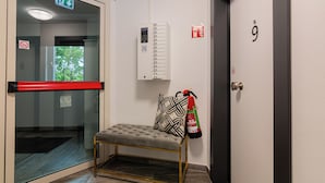 Entrada de hotel con puerta de cristal, extintor, banco y cartel con número de habitación.