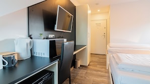 Una habitación de hotel moderna con kitchenette, un televisor de pantalla plana montado en la pared, una cama con sábanas blancas y piso de madera.