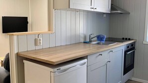 A compact kitchen with white cabinetry, a wooden countertop, a built-in dishwasher, a stove, and a sink. - Vollanvegen 13 (Mosjøen)