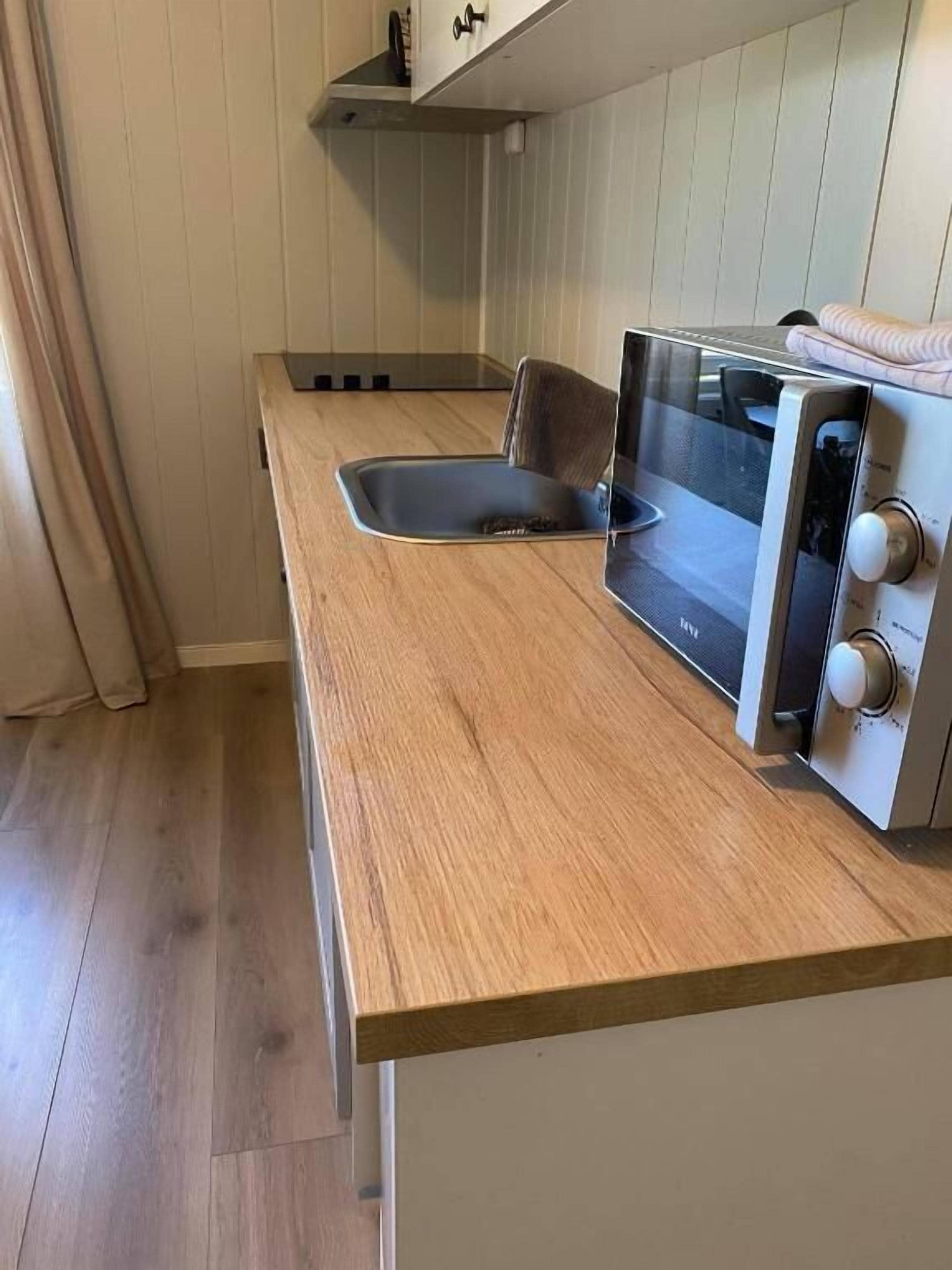 A compact kitchen with a wooden countertop, a built-in microwave, and a sink.