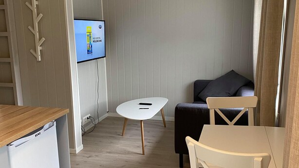 A compact room with a kitchenette, a small round table, a sofa, and a TV mounted on the wall. - Vollanvegen 13 (Mosjøen)