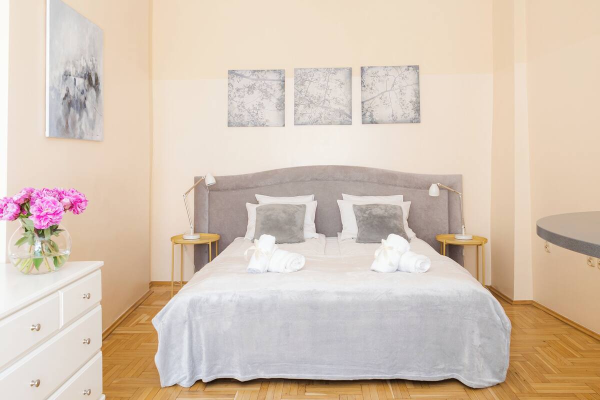 A neatly arranged bedroom with a large bed, two bedside tables, a dresser, and a vase of flowers.