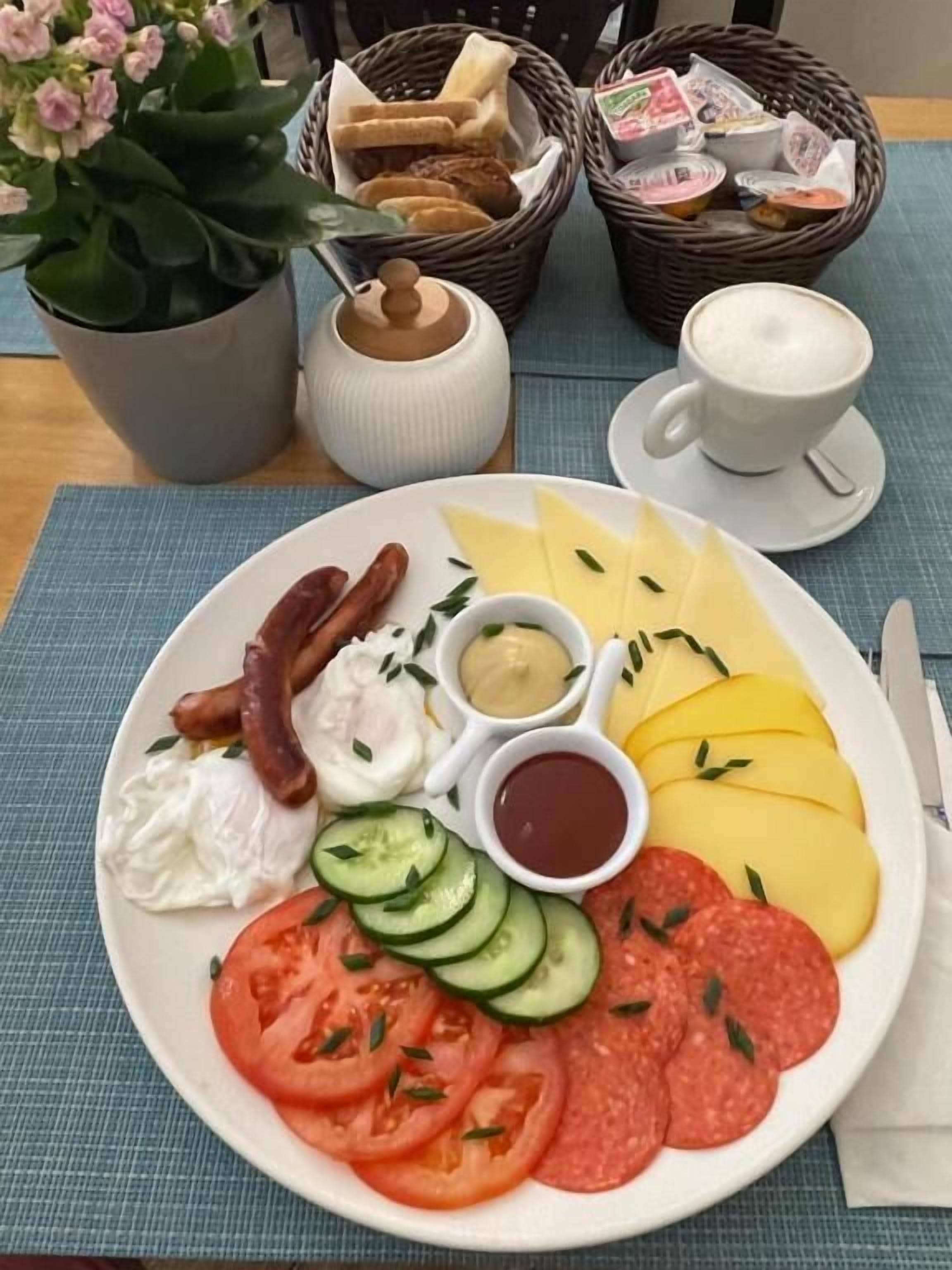 A breakfast plate with eggs, sausages, cheese, tomatoes, cucumbers, and condiments.
